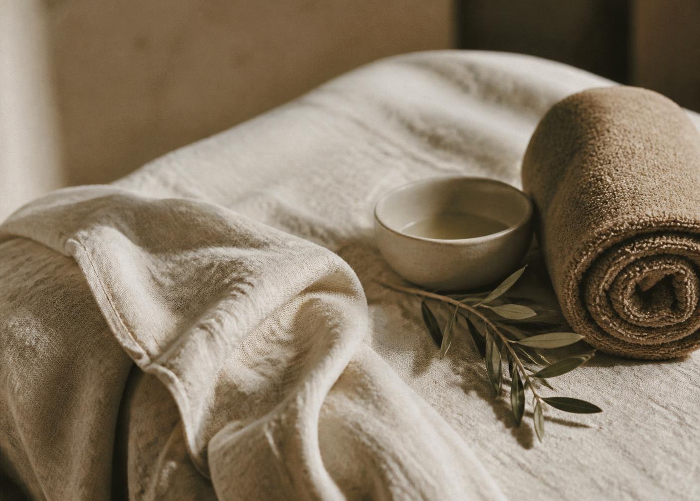 Soft linens, a ceramic bowl of oil, warm towel and olive sprig