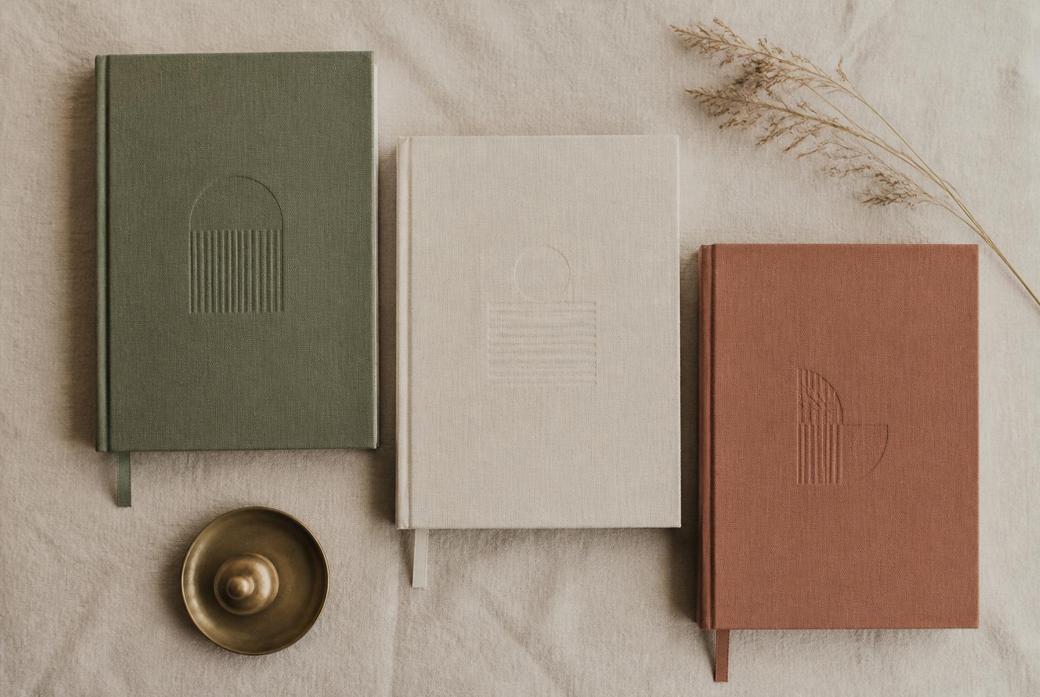 Three linen-bound LETHEN journals in sage, cream and clay on natural linen